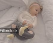 Active baby girl of six months old lying on bed and pulling her sock. Indoor shot of blue-eyed child with a bow, top viewnLicense this clip: https://fillerstock.com/video/13609