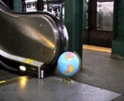 The handrail of a New York City subway escalator presses up against a desktop globe, making the world turn.